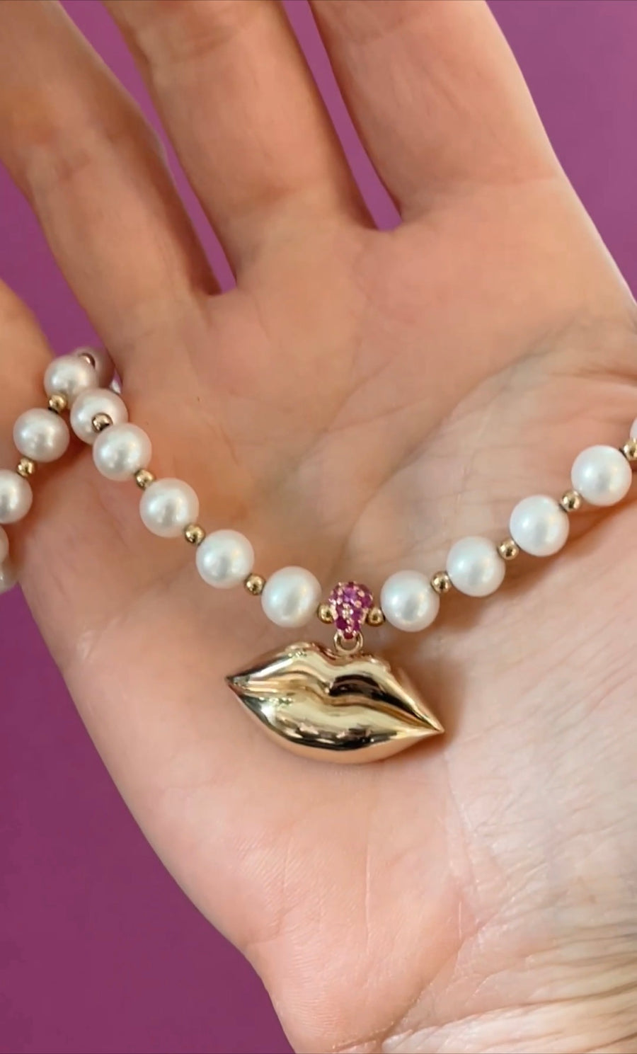 view of pearl necklace with a sparkling bail of magenta sapphires to add an extra pop of color in the palm of a hand on a pink background