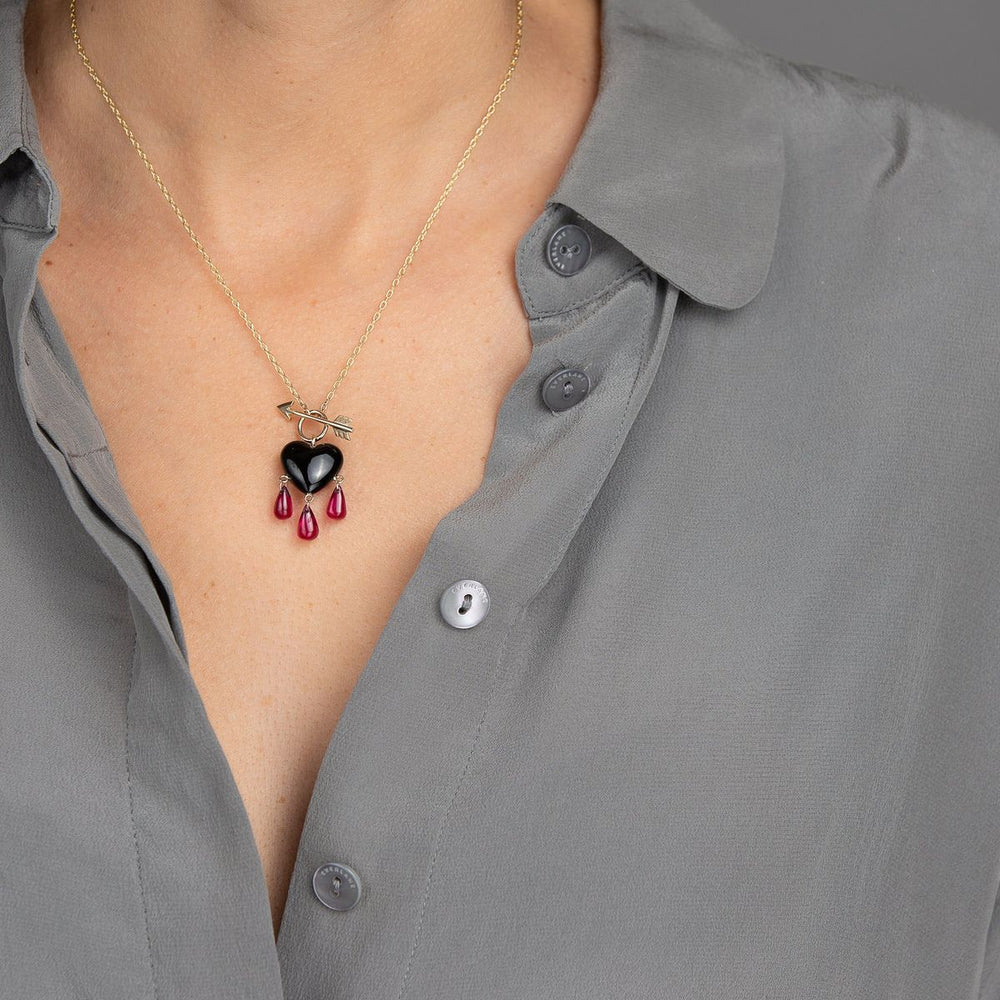 woman in grey modeling small smooth jet black onyx charm necklace drips with a trio of ruby blood with gold arrow toggle closure on yellow chain necklace