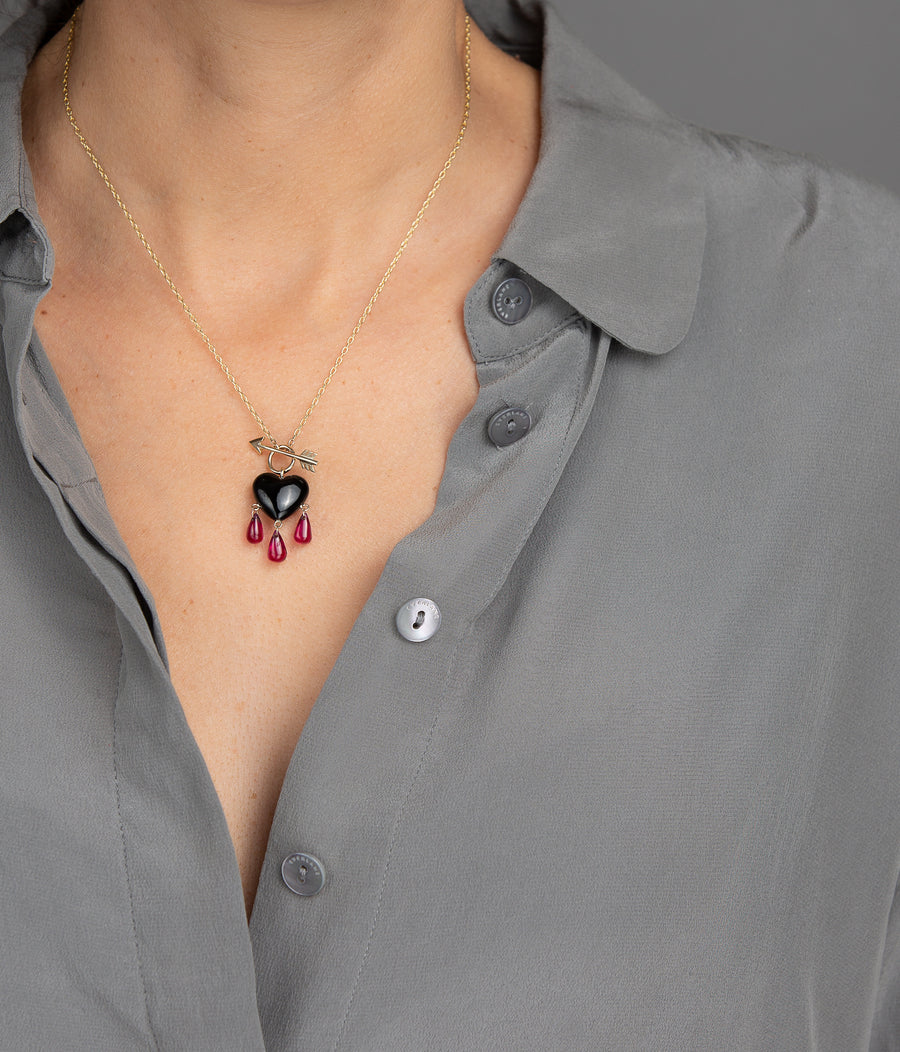 woman in grey modeling small smooth jet black onyx charm necklace drips with a trio of ruby blood with gold arrow toggle closure on yellow chain necklace