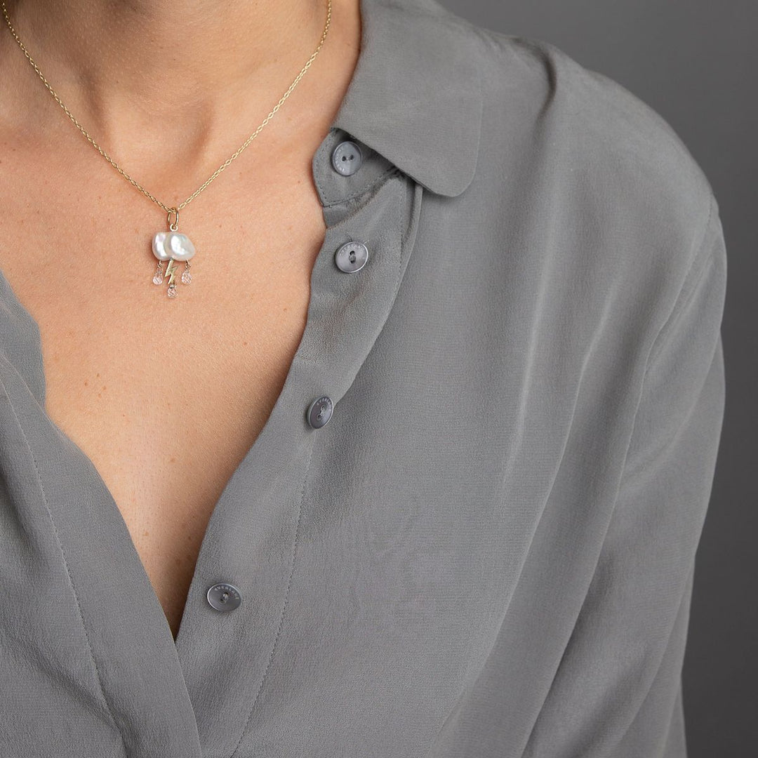 woman in grey modeling small keshi cloud like pearl charm with 3 white topaz rain drops from underneath and yellow gold lightening bolt of the center three on gold chain necklace