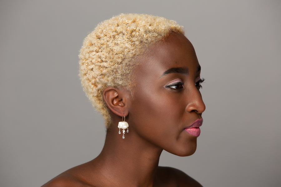 woman modeling a single white stormy keshi cloud like pearl earring with 14K yellow gold lightning bolt as a trio of white topaz rain down with gold ear wire