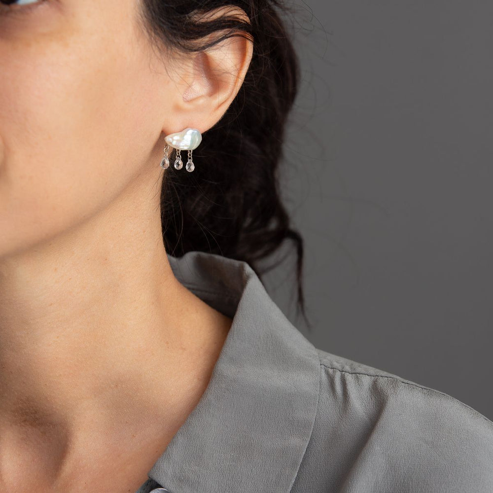 woman in grey modeling white keshi pearl earrings in cloud-like form with three white topaz dangling from the bottom with yellow gold components