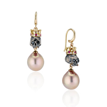 set of regal skull earrings are bejeweled with 14K gold crowns set with brilliant cut rubies and diamonds all around. Twinkling black diamond eyes and a single front gold tooth set on a white background