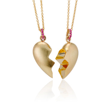 angled view of pair of shared heart puffy necklaces made in 14k yellow gold with a brushed finish but shiny interior finish where heart is cut in half jagged. Rubies on bail in gold necklace chain