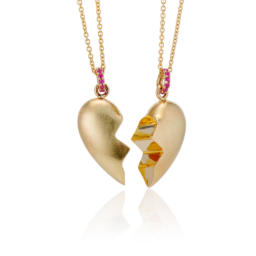 angled view of pair of shared heart puffy necklaces made in 14k yellow gold with a brushed finish but shiny interior finish where heart is cut in half jagged. Rubies on bail in gold necklace chain