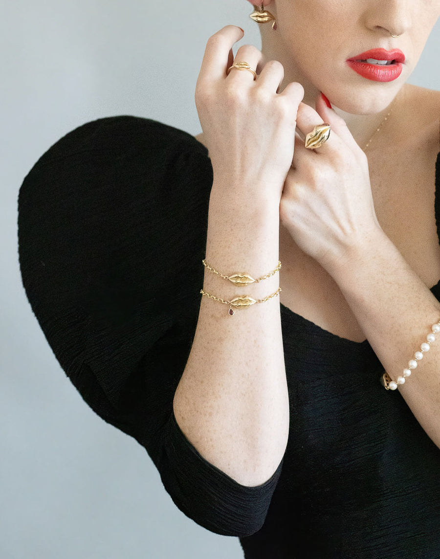 model in chic black dress wearing gold lip earrings, rings, bracelets, and necklace