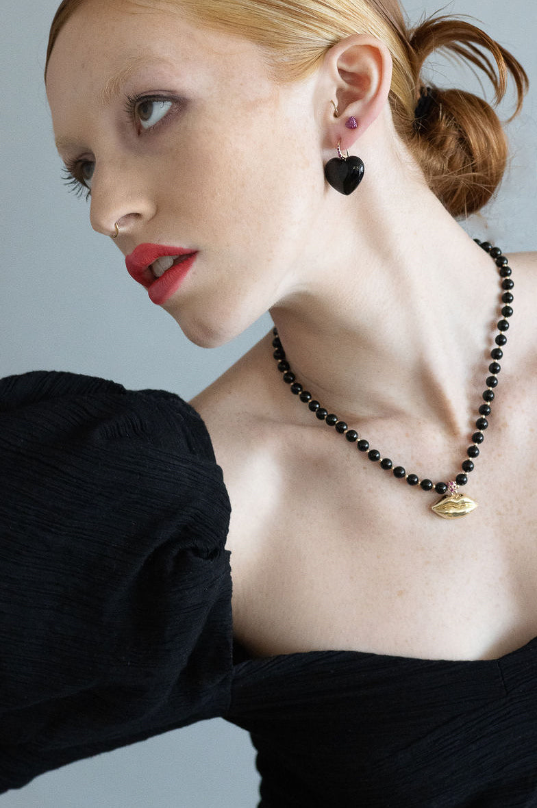 red head model wearing black heart earrings and gold & black lip necklace