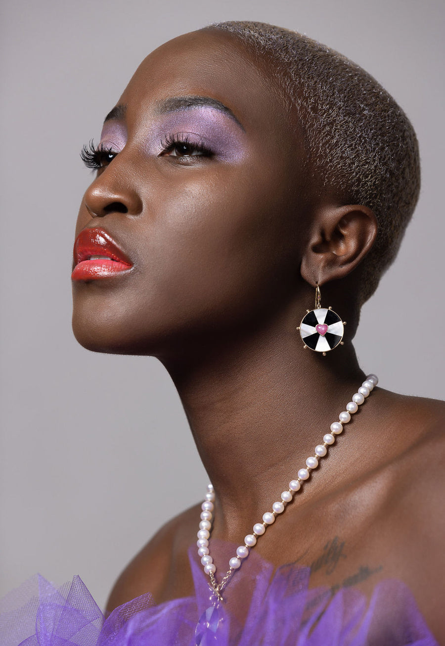 black model on a grey background with shaved head wearing purple and both bullseye heart necklace and earrings