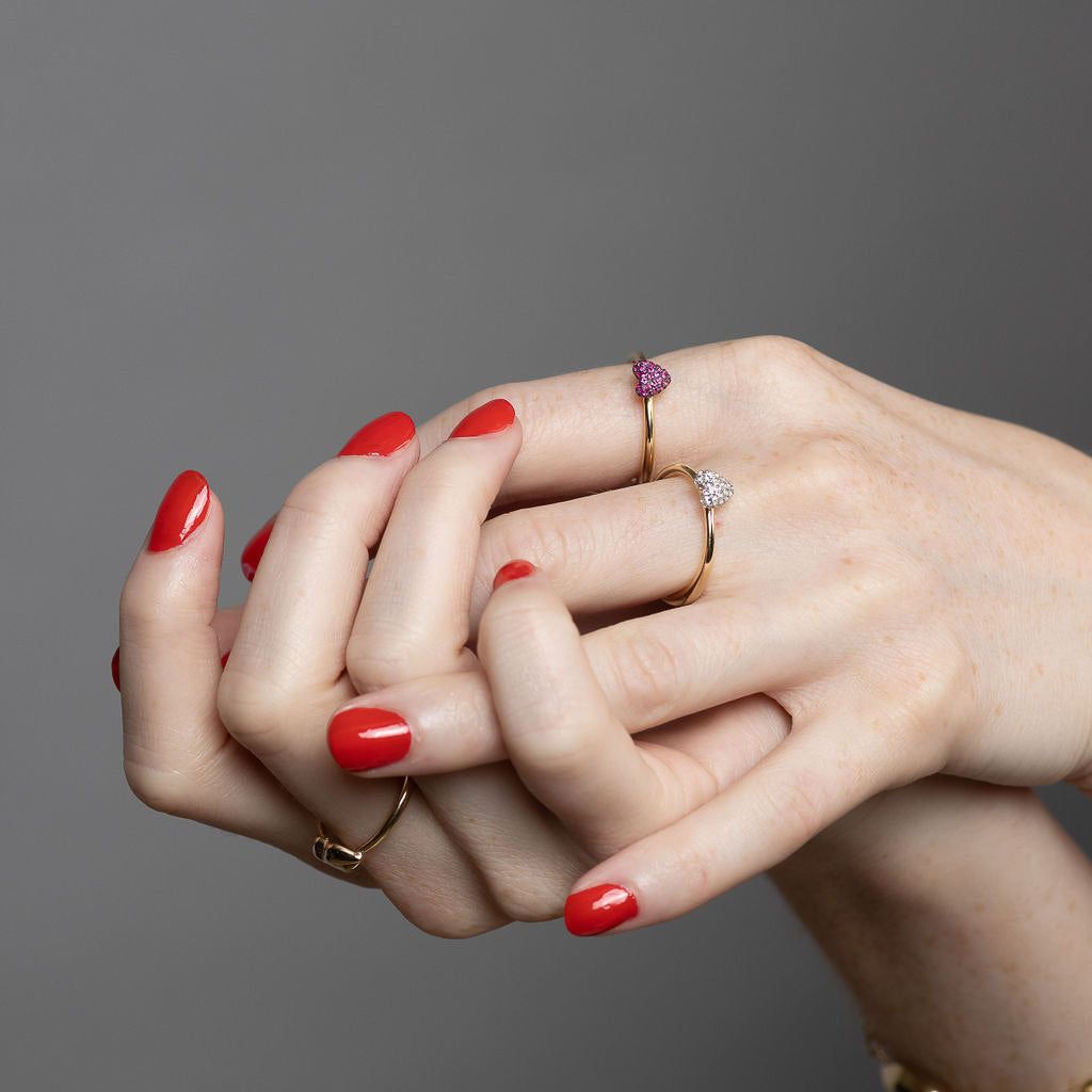 model holding her own hands with red nail polish wearing the sweet p heart rings on a grey background